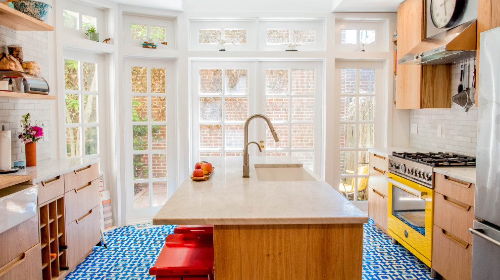 This is an example of an eclectic galley kitchen in Philadelphia with a farmhouse sink, beige cabinets, white splashback, coloured appliances, cement tiles, blue floor and white benchtop.