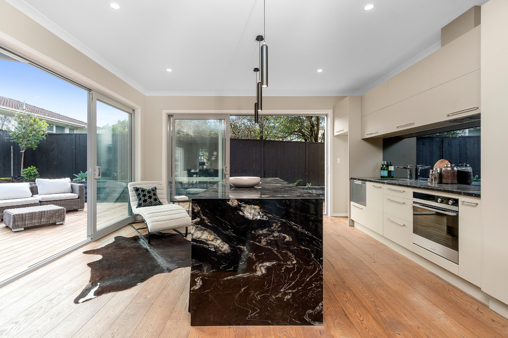 Galley open plan kitchen in Auckland with flat-panel cabinets, grey cabinets, marble benchtops, black splashback, stainless steel appliances, light hardwood floors and with island.