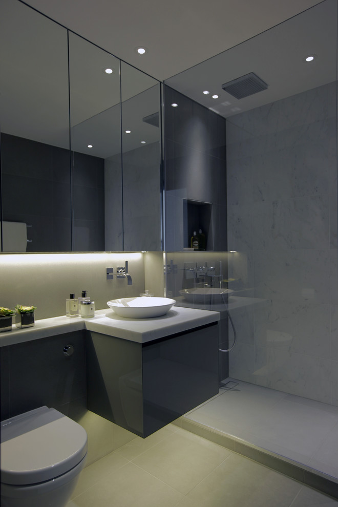 Small contemporary 3/4 bathroom in London with grey cabinets, a curbless shower, a wall-mount toilet, gray tile, stone tile, grey walls, marble floors, a vessel sink and marble benchtops.