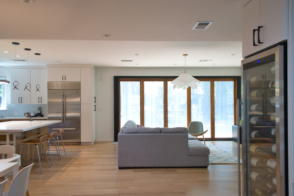 На фото: большая открытая гостиная комната в стиле модернизм с домашним баром, белыми стенами, светлым паркетным полом, коричневым полом и отдельно стоящим телевизором без камина