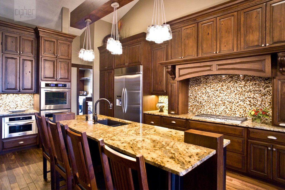 Example of a mid-sized transitional l-shaped medium tone wood floor and brown floor eat-in kitchen design with an undermount sink, dark wood cabinets, multicolored backsplash, stainless steel appliances, beige walls, an island, raised-panel cabinets, granite countertops and mosaic tile backsplash