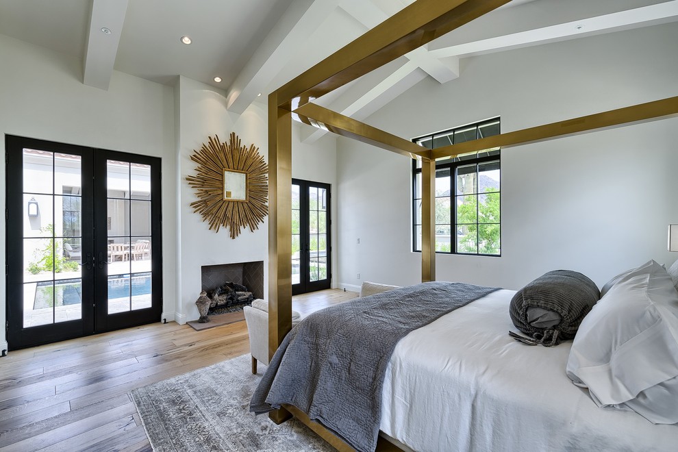 Inspiration for a large mediterranean master bedroom in Phoenix with white walls, medium hardwood floors, a standard fireplace, a plaster fireplace surround and brown floor.