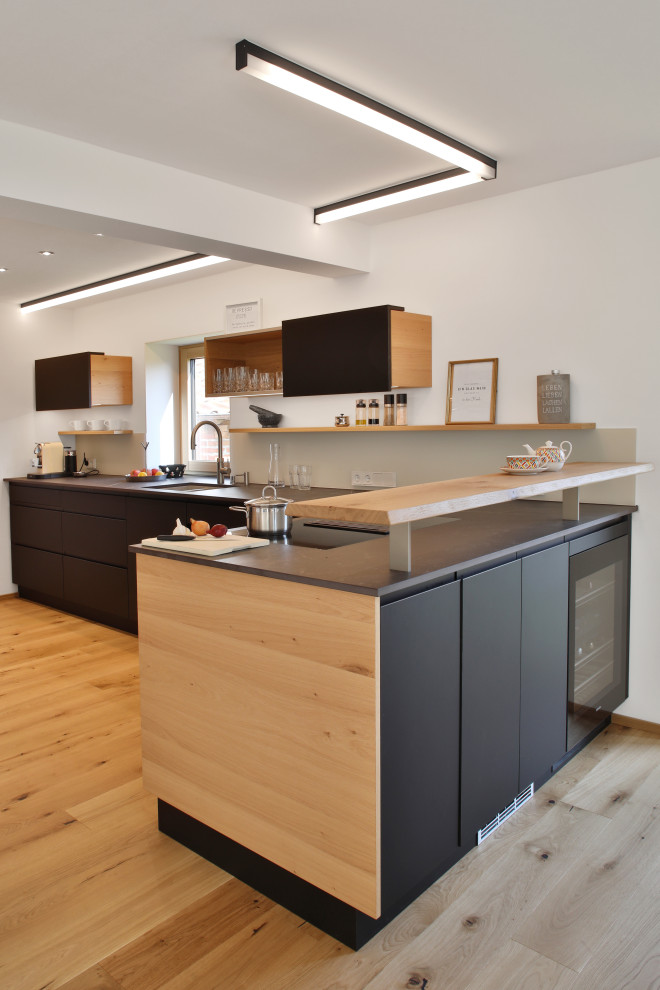 Photo of a contemporary l-shaped kitchen in Munich with an undermount sink, flat-panel cabinets, black cabinets, medium hardwood floors, a peninsula, brown floor and grey benchtop.