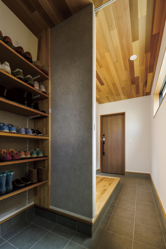 На фото: прихожая со шкафом для обуви в стиле модернизм с белыми стенами, полом из керамической плитки, входной дверью из дерева среднего тона, черным полом, деревянным потолком и обоями на стенах