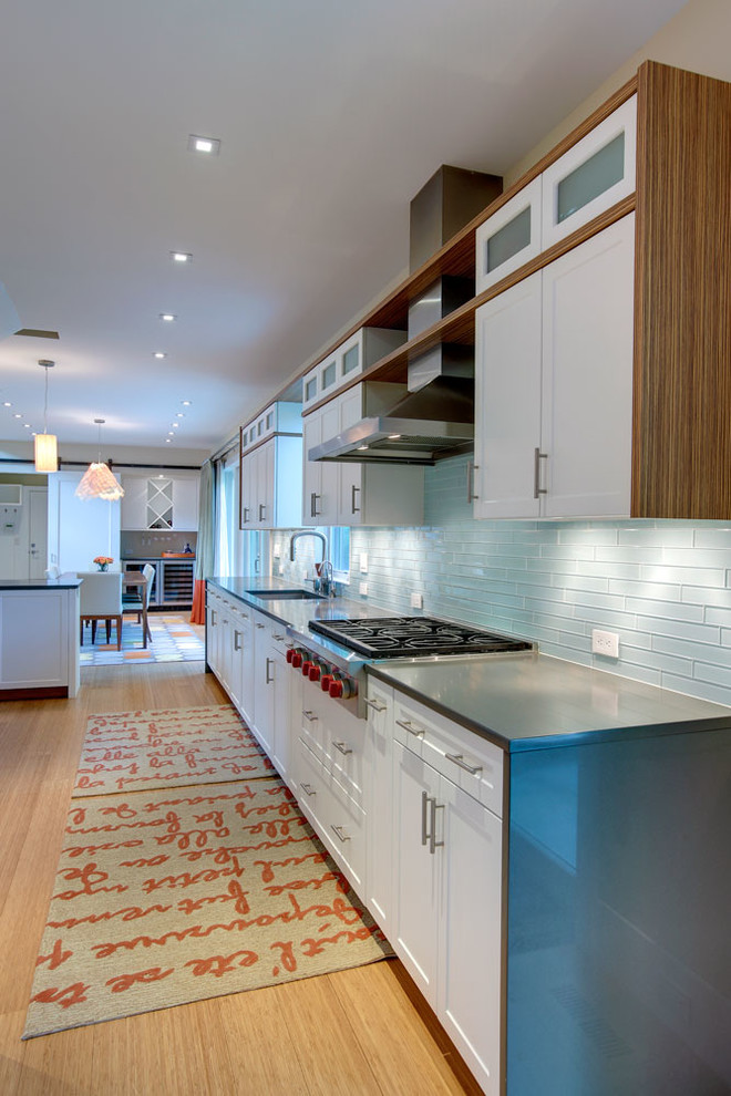Photo of a large contemporary galley open plan kitchen in New York with an undermount sink, flat-panel cabinets, white cabinets, blue splashback, subway tile splashback, stainless steel appliances, light hardwood floors and a peninsula.