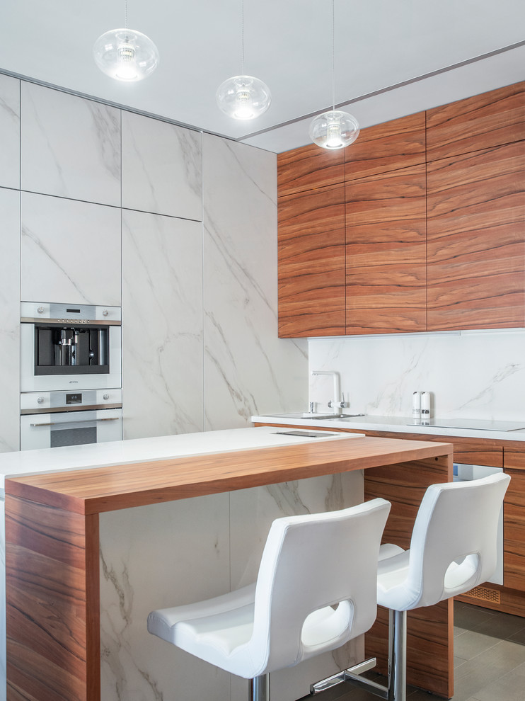 This is an example of a contemporary l-shaped kitchen in Moscow with flat-panel cabinets, medium wood cabinets, white splashback, white appliances, with island, grey floor and white benchtop.