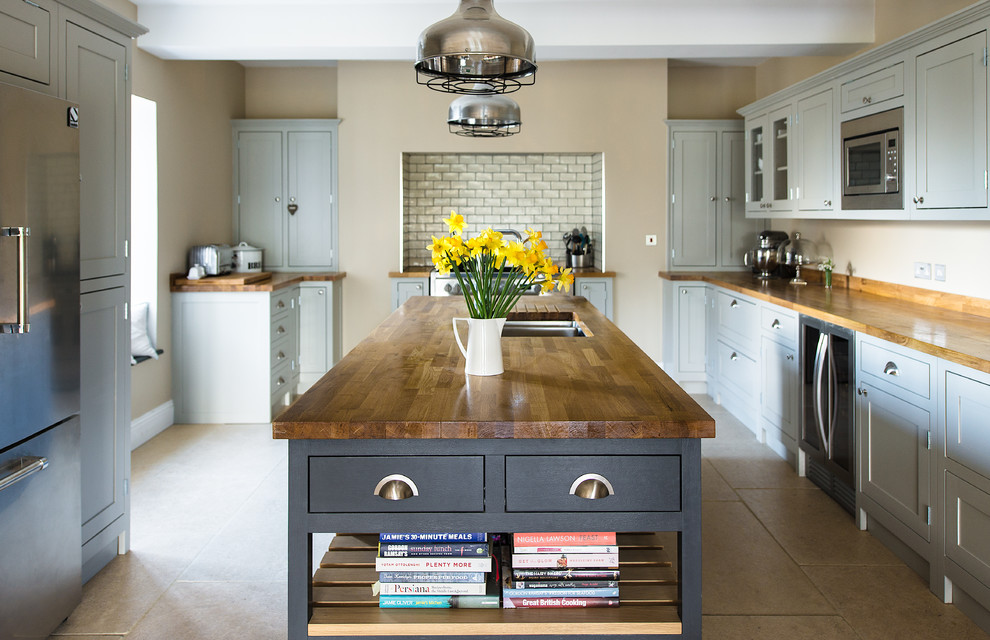 This is an example of a mid-sized transitional open plan kitchen in Gloucestershire with shaker cabinets, wood benchtops, grey splashback, ceramic splashback, stainless steel appliances, with island, an undermount sink and grey cabinets.