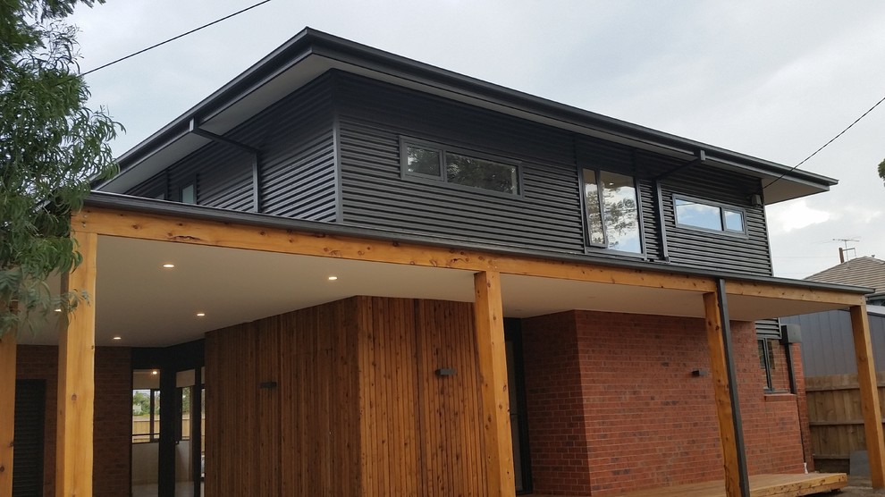 Photo of a large industrial two-storey black house exterior in Melbourne with a metal roof, metal siding and a hip roof.