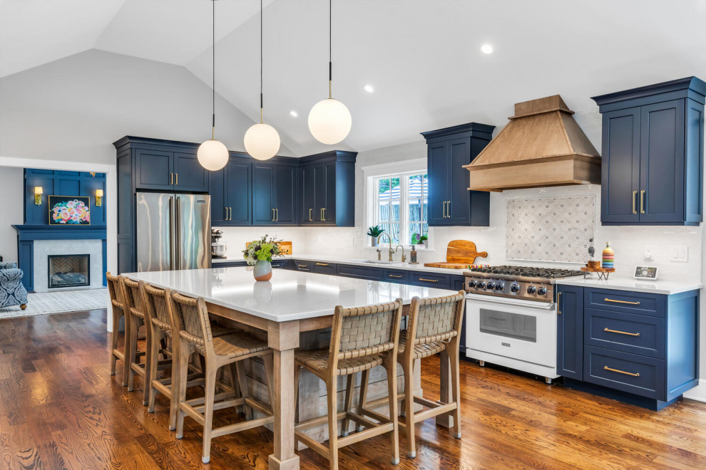This is an example of a large transitional l-shaped eat-in kitchen in New York with an undermount sink, flat-panel cabinets, blue cabinets, quartz benchtops, white splashback, porcelain splashback, stainless steel appliances, medium hardwood floors, brown floor, white benchtop and vaulted.
