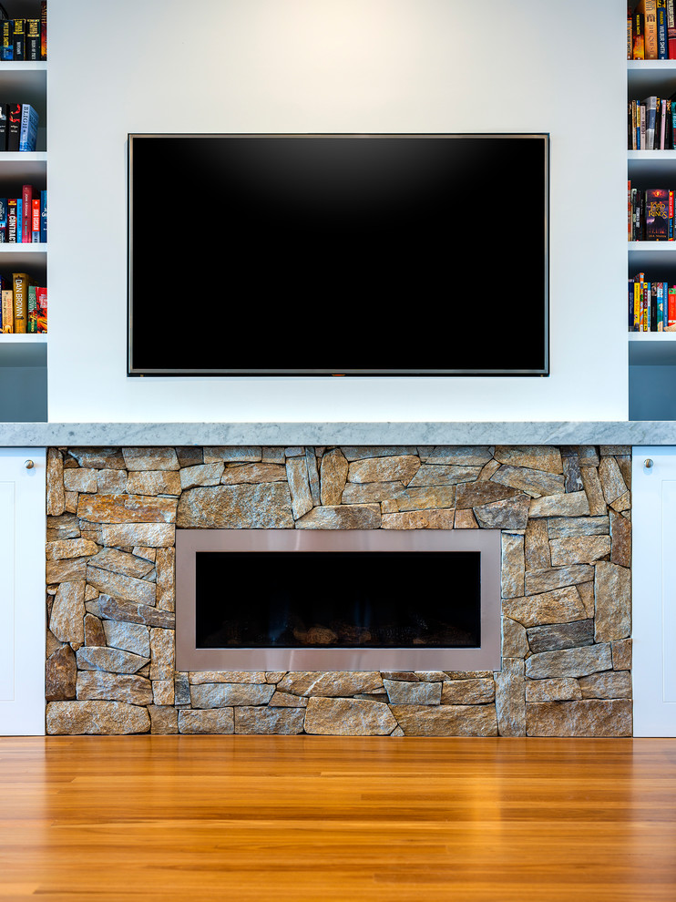 Photo of a beach style living room in Central Coast with a library, medium hardwood floors, a standard fireplace, a stone fireplace surround and a built-in media wall.