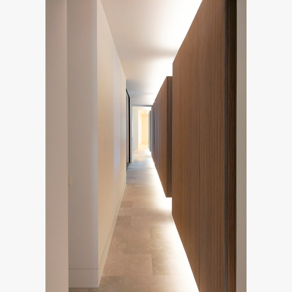 На фото: большой коридор: освещение в стиле модернизм с белыми стенами, полом из известняка, бежевым полом и панелями на стенах с