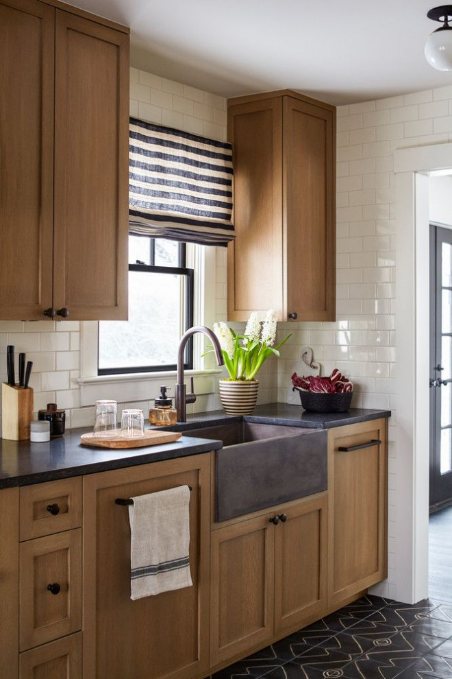 Inspiration for a mid-sized contemporary l-shaped eat-in kitchen in Columbus with a farmhouse sink, shaker cabinets, medium wood cabinets, soapstone benchtops, white splashback, subway tile splashback, white appliances, ceramic floors, black floor and grey benchtop.