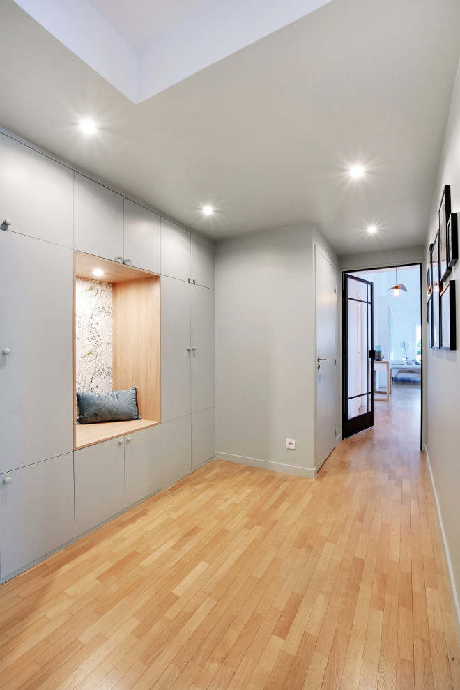Cette image montre un grand hall d'entrée minimaliste avec un mur vert, un sol en bois brun, une porte simple et un sol marron.