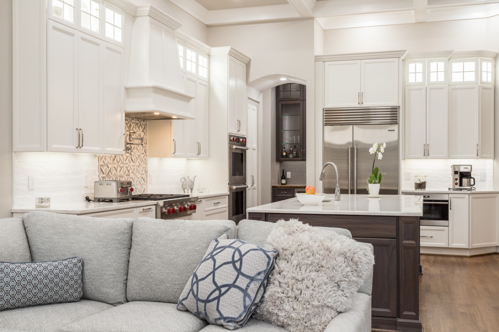 Photo of a large transitional u-shaped open plan kitchen in Raleigh with shaker cabinets, white cabinets, quartz benchtops, white splashback, subway tile splashback, stainless steel appliances, medium hardwood floors, with island and coffered.