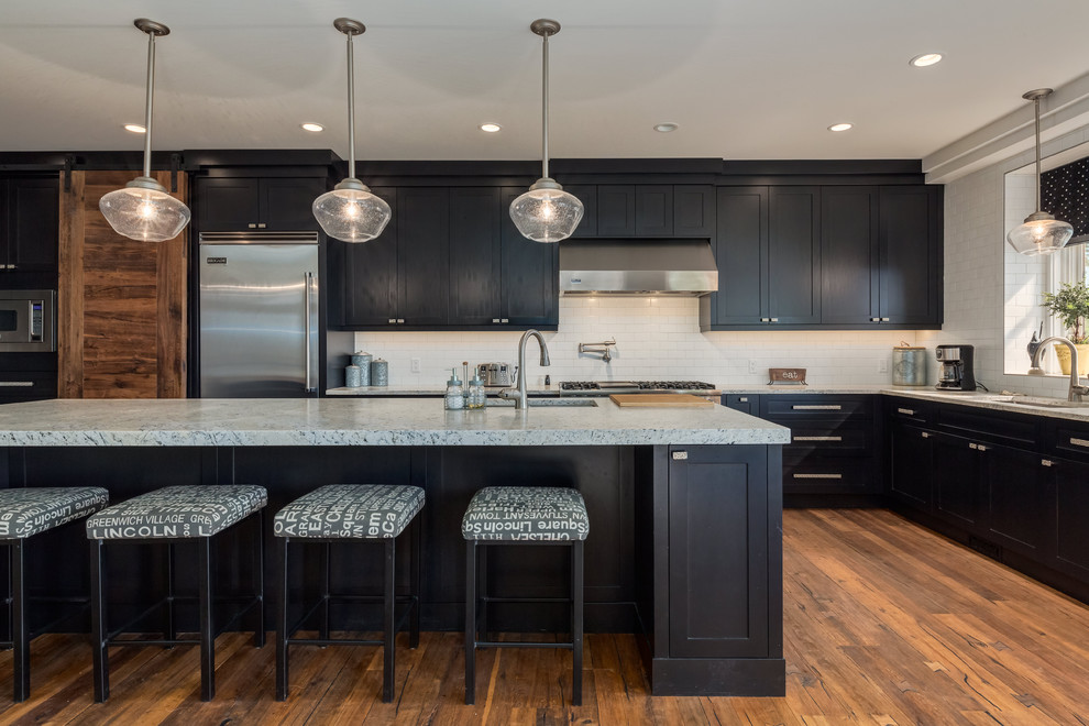 Example of a huge transitional u-shaped medium tone wood floor and brown floor kitchen design in Calgary with an undermount sink, shaker cabinets, black cabinets, white backsplash, ceramic backsplash, stainless steel appliances, an island and granite countertops