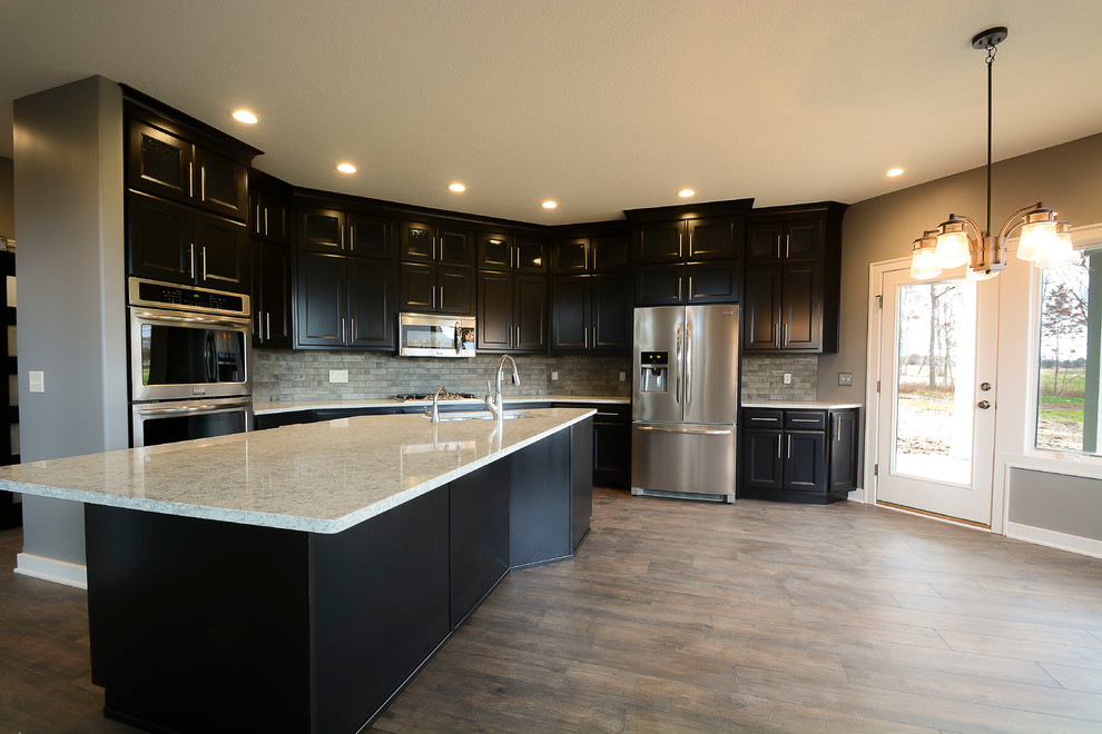 Large transitional l-shaped dark wood floor and brown floor open concept kitchen photo with an island, shaker cabinets, gray backsplash, a double-bowl sink, stainless steel appliances and black cabinets