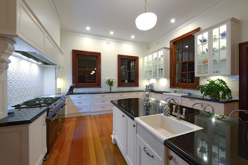 Photo of an expansive victorian u-shaped eat-in kitchen in Newcastle - Maitland with a farmhouse sink, recessed-panel cabinets, white cabinets, granite benchtops, white splashback, subway tile splashback, medium hardwood floors and with island.