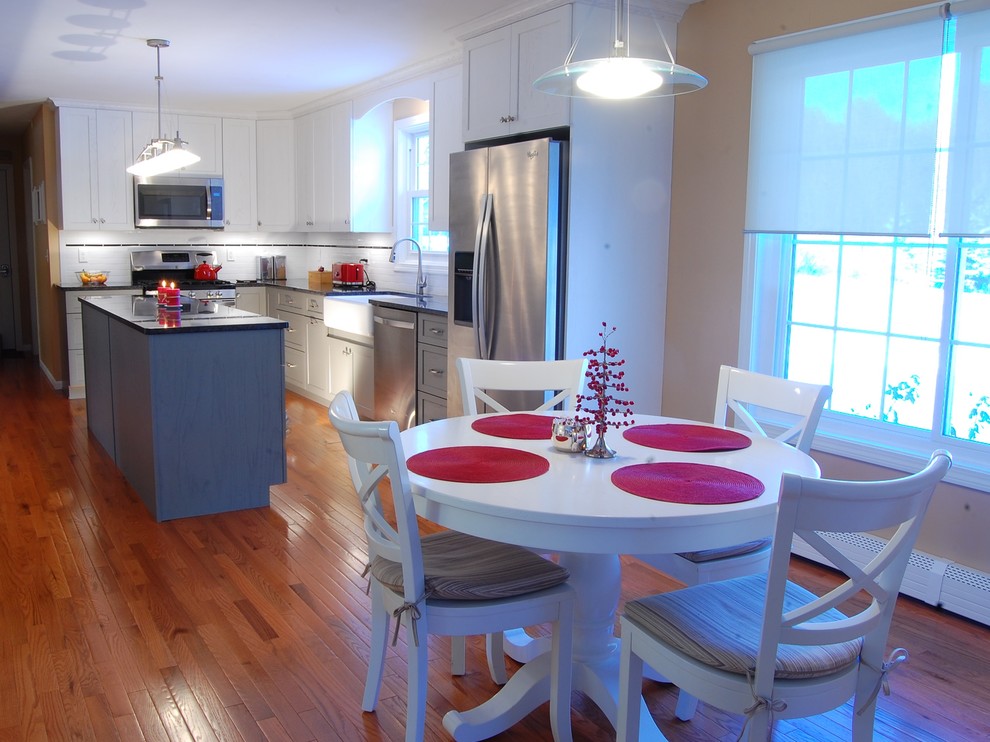 Inspiration for a mid-sized transitional l-shaped medium tone wood floor eat-in kitchen remodel in Boston with a farmhouse sink, shaker cabinets, white cabinets, quartz countertops, white backsplash, subway tile backsplash, stainless steel appliances and an island