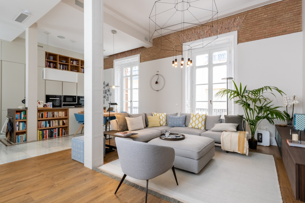 Foto de biblioteca en casa abierta contemporánea con paredes blancas, suelo de madera en tonos medios, televisor colgado en la pared, suelo marrón y ladrillo