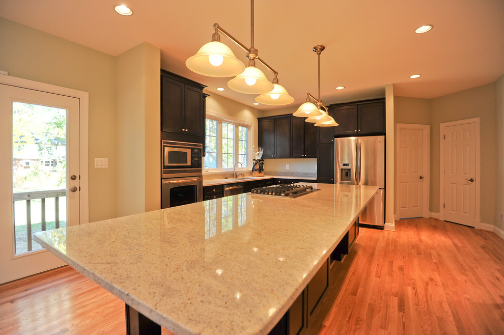 Open concept kitchen - l-shaped medium tone wood floor open concept kitchen idea in DC Metro with an undermount sink, recessed-panel cabinets, dark wood cabinets, granite countertops, stainless steel appliances and an island