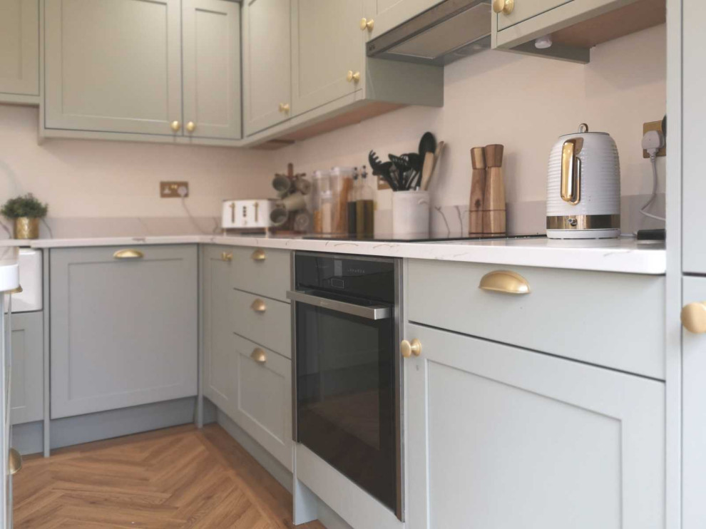 Design ideas for a medium sized traditional l-shaped open plan kitchen in Other with a belfast sink, shaker cabinets, green cabinets, quartz worktops, black appliances, an island and white worktops.
