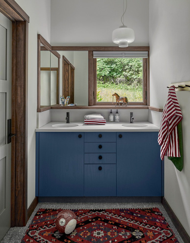 Small rustic family bathroom in Chicago with flat-panel cabinets, blue cabinets, white walls, a submerged sink, grey floors, white worktops, double sinks, a built in vanity unit, an alcove bath, a shower/bath combination, a one-piece toilet, terrazzo flooring, solid surface worktops, a shower curtain, an enclosed toilet and a vaulted ceiling.