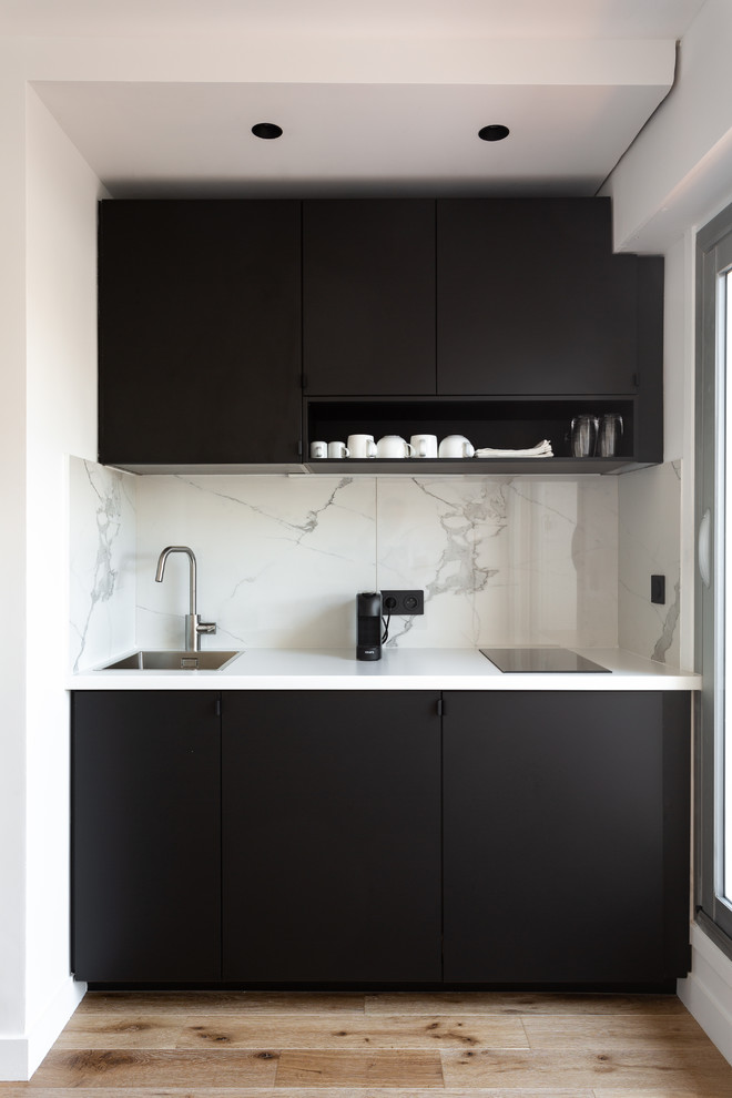 This is an example of a small contemporary single-wall open plan kitchen in London with a drop-in sink, flat-panel cabinets, black cabinets, marble benchtops, white splashback, marble splashback, panelled appliances, light hardwood floors, no island, beige floor and white benchtop.