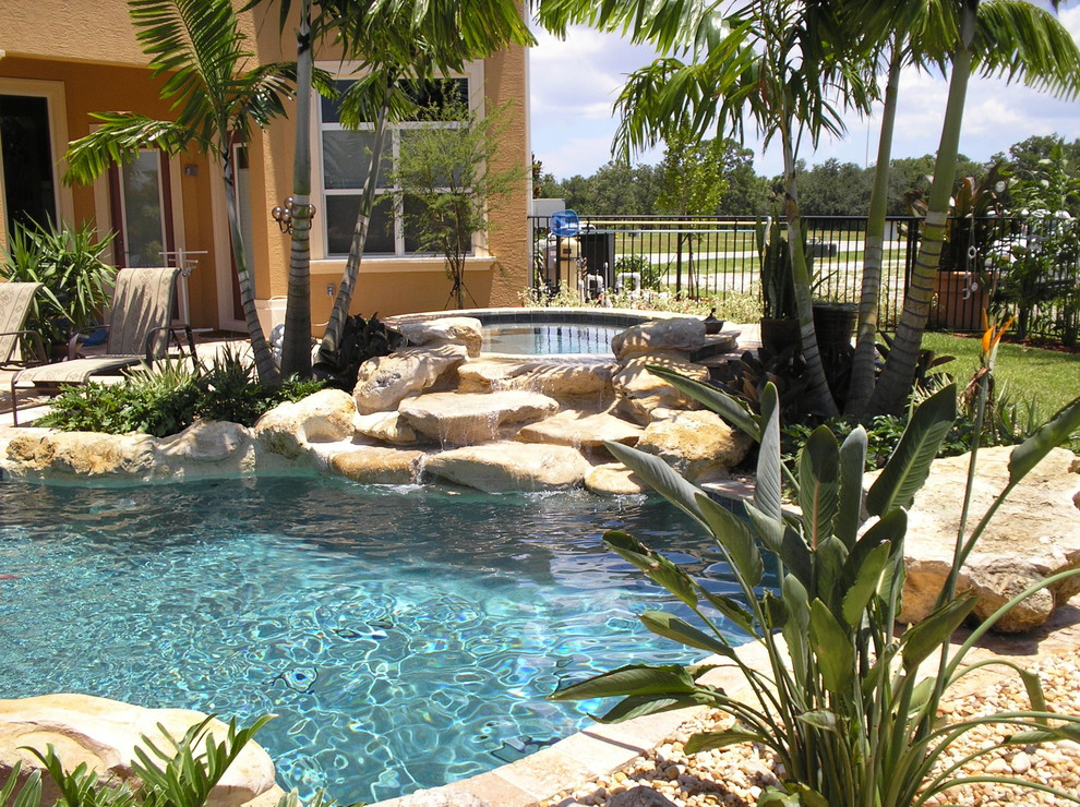 Large tropical backyard custom-shaped pool in Miami with a water feature and gravel.