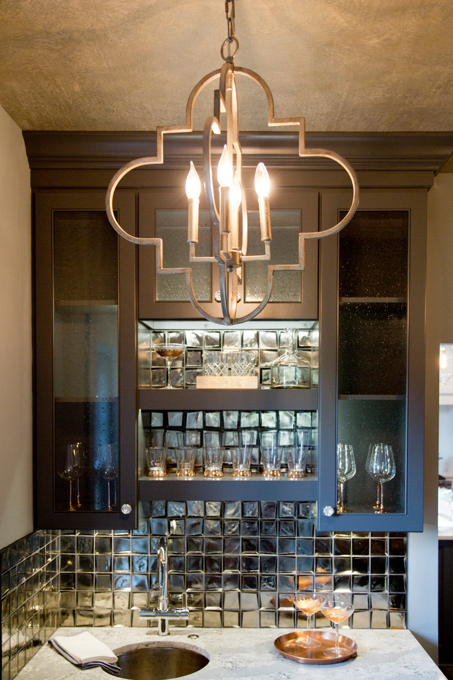 This is an example of a mid-sized transitional galley wet bar in Kansas City with glass-front cabinets, grey cabinets, granite benchtops, metal splashback, dark hardwood floors and brown floor.