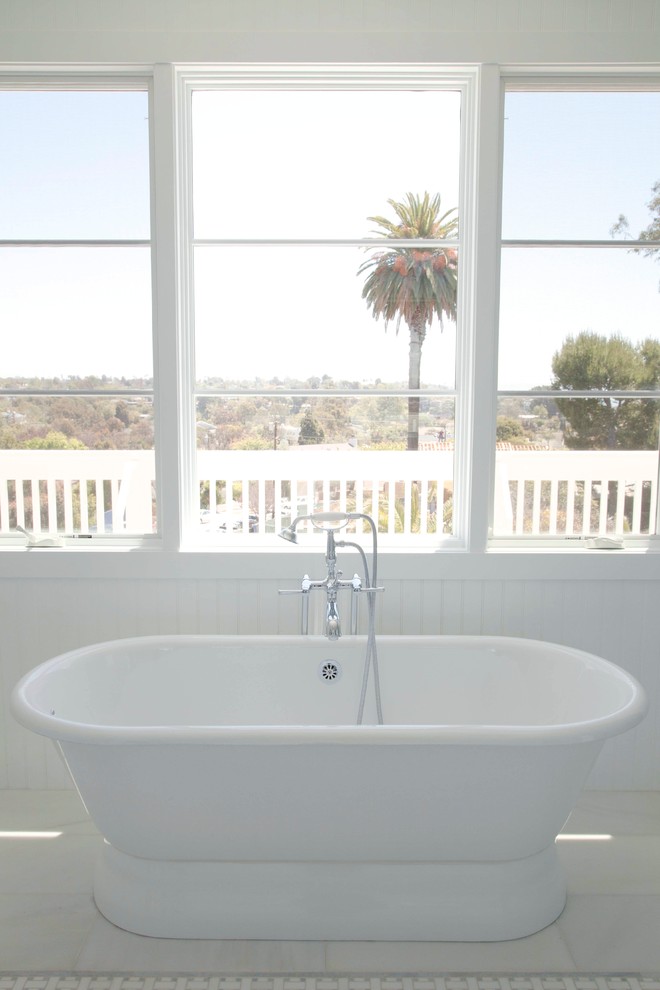 Inspiration for a large beach style master bathroom in Los Angeles with an undermount sink, shaker cabinets, white cabinets, marble benchtops, a freestanding tub, a corner shower, a one-piece toilet, white tile, stone tile, white walls and marble floors.