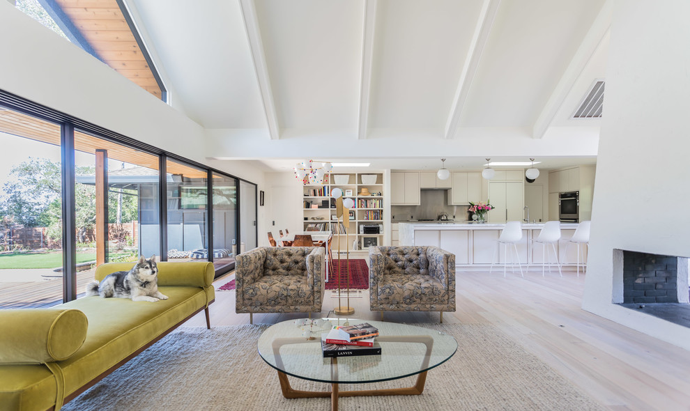 Midcentury open concept living room in San Francisco with white walls, light hardwood floors, a two-sided fireplace and a plaster fireplace surround.