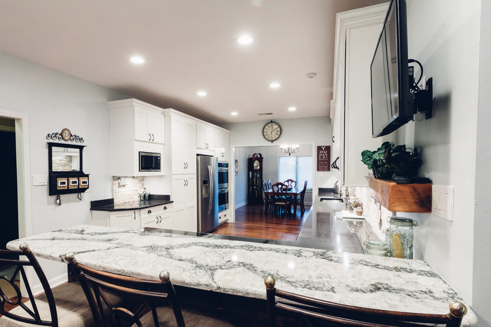 Large transitional galley light wood floor and brown floor open concept kitchen photo with an undermount sink, shaker cabinets, white cabinets, quartz countertops, white backsplash, stone tile backsplash, stainless steel appliances and a peninsula