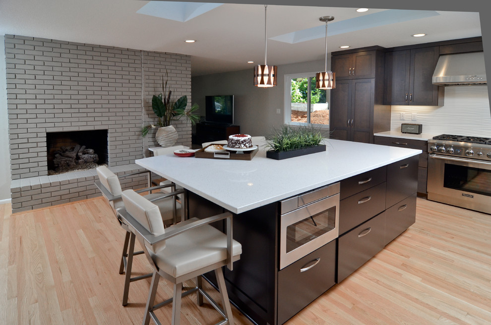 Photo of a large transitional kitchen in Portland with an undermount sink, shaker cabinets, dark wood cabinets, quartz benchtops, white splashback, porcelain splashback, stainless steel appliances, light hardwood floors and with island.