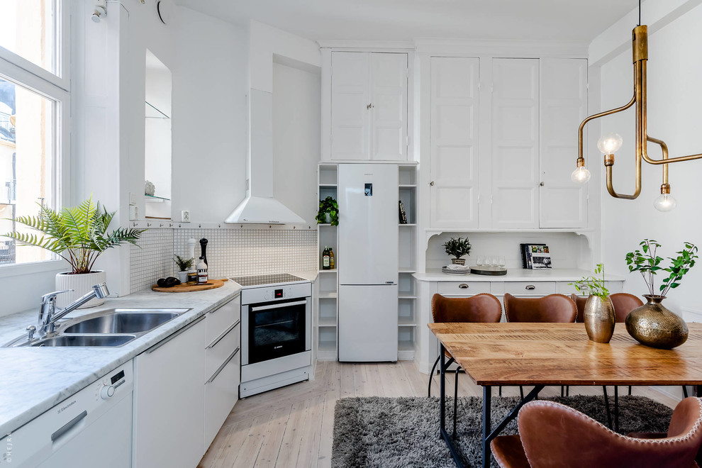 Design ideas for a scandinavian l-shaped eat-in kitchen in Stockholm with a double-bowl sink, recessed-panel cabinets, white cabinets, white splashback, white appliances, light hardwood floors, no island, beige floor and grey benchtop.