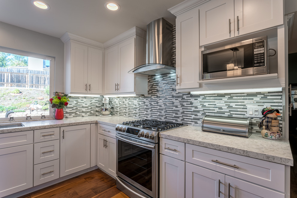 Inspiration for a mid-sized transitional l-shaped eat-in kitchen in San Diego with an undermount sink, shaker cabinets, white cabinets, grey splashback, matchstick tile splashback, stainless steel appliances, medium hardwood floors, with island, brown floor and grey benchtop.