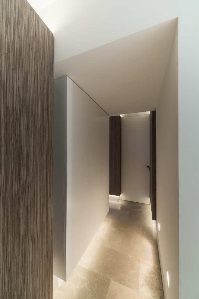 Пример оригинального дизайна: большой коридор: освещение в стиле модернизм с белыми стенами, полом из известняка, бежевым полом и панелями на стенах