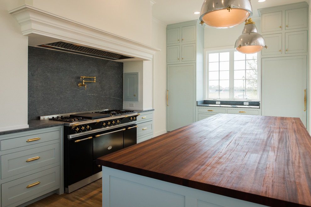Large transitional u-shaped light wood floor and brown floor kitchen photo in Dallas with a farmhouse sink, recessed-panel cabinets, black backsplash, ceramic backsplash, black appliances, an island and brown countertops