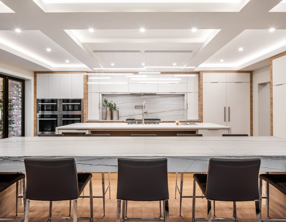Photo of a large contemporary single-wall open plan kitchen in Vancouver with a belfast sink, flat-panel cabinets, light wood cabinets, quartz worktops, white splashback, marble splashback, stainless steel appliances, medium hardwood flooring, multiple islands, brown floors, white worktops and a coffered ceiling.