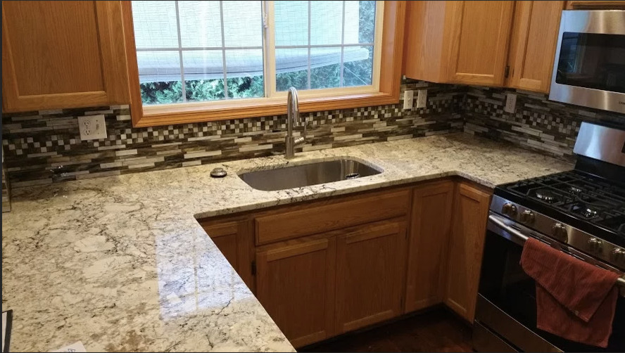 Mid-sized transitional u-shaped medium tone wood floor kitchen photo in Seattle with an undermount sink, recessed-panel cabinets, light wood cabinets, granite countertops, multicolored backsplash, matchstick tile backsplash, stainless steel appliances and no island