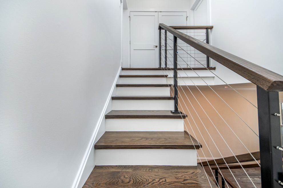 На фото: огромная п-образная лестница в современном стиле с деревянными ступенями, крашенными деревянными подступенками и перилами из тросов