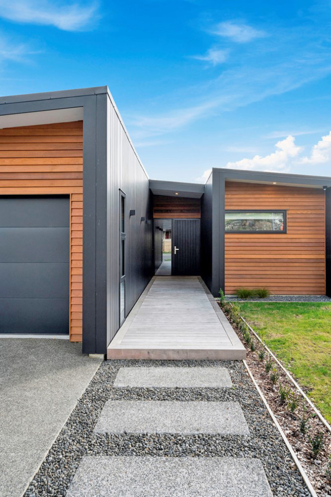 Стильный дизайн: большой, одноэтажный, деревянный, коричневый частный загородный дом с плоской крышей, металлической крышей, черной крышей и отделкой планкеном - последний тренд