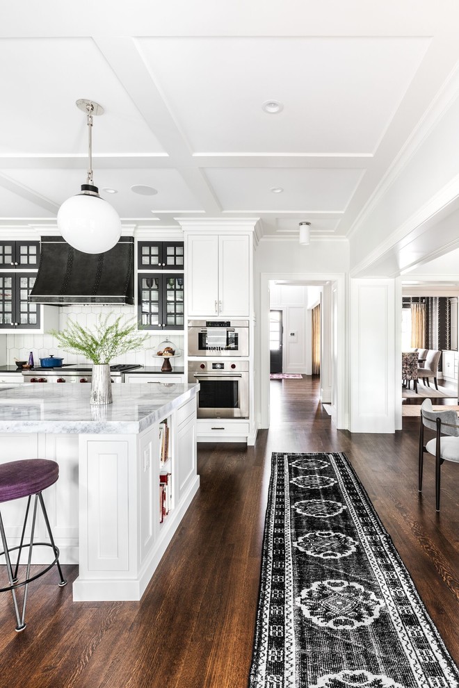 This is an example of a large transitional open plan kitchen in Chicago with beaded inset cabinets, white cabinets, medium hardwood floors, brown floor, an undermount sink, granite benchtops, panelled appliances, black benchtop and with island.