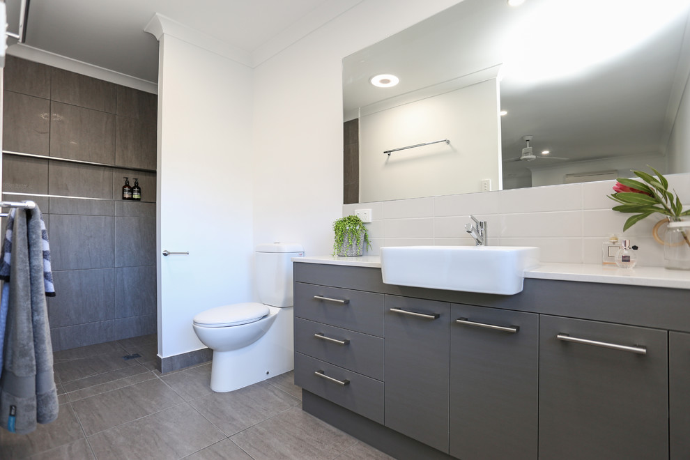 Photo of a mid-sized scandinavian kids bathroom with flat-panel cabinets, grey cabinets, a freestanding tub, an open shower, gray tile, ceramic tile, white walls, ceramic floors, engineered quartz benchtops, grey floor and an open shower.