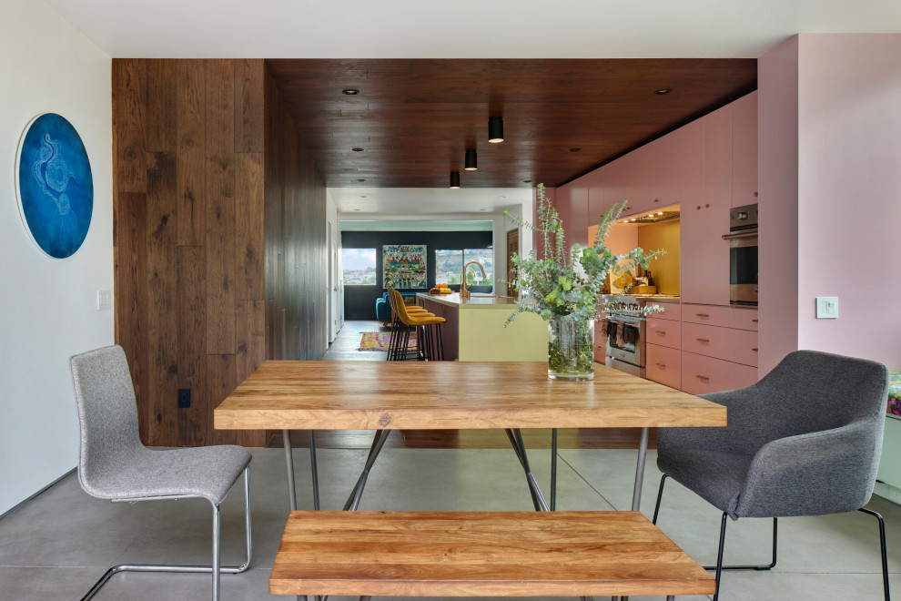 Ispirazione per una sala da pranzo aperta verso la cucina mediterranea di medie dimensioni con pareti rosa, pavimento in cemento, nessun camino, pavimento grigio, pareti in legno e soffitto in legno
