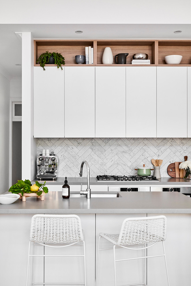 This is an example of a mid-sized modern galley eat-in kitchen in Sydney with an undermount sink, white cabinets, quartz benchtops, white splashback, stone tile splashback, black appliances, medium hardwood floors, with island, brown floor and grey benchtop.