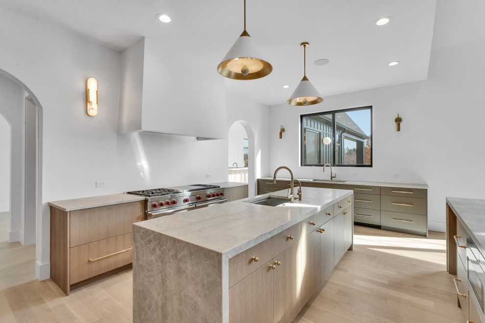 Example of a large transitional u-shaped light wood floor, beige floor and vaulted ceiling open concept kitchen design with an undermount sink, flat-panel cabinets, light wood cabinets, quartzite countertops, white backsplash, paneled appliances, two islands and beige countertops