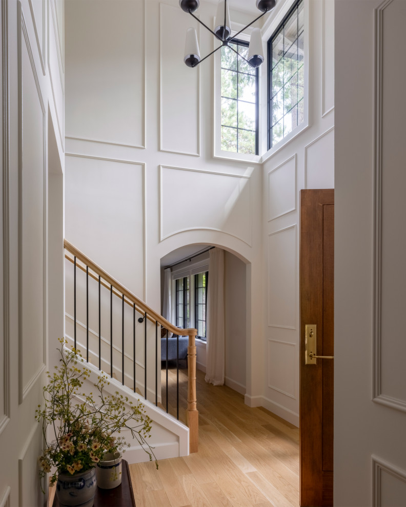 Example of a large classic light wood floor, vaulted ceiling and wainscoting foyer design in Seattle with white walls and a dark wood front door