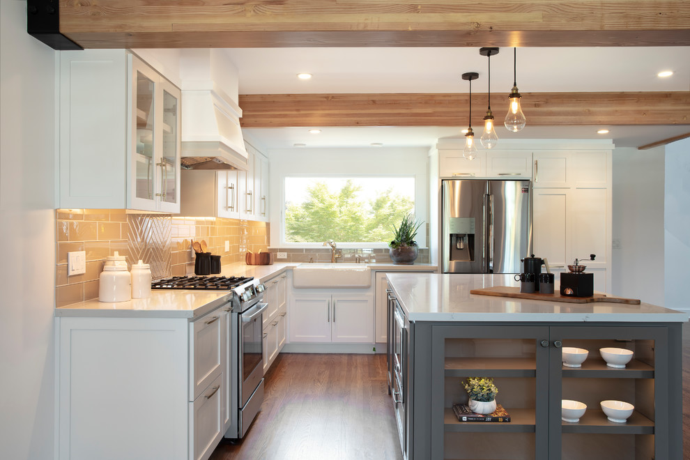 This is an example of a mid-sized transitional l-shaped open plan kitchen in San Francisco with a farmhouse sink, shaker cabinets, white cabinets, quartzite benchtops, beige splashback, ceramic splashback, stainless steel appliances, medium hardwood floors, with island, brown floor and white benchtop.