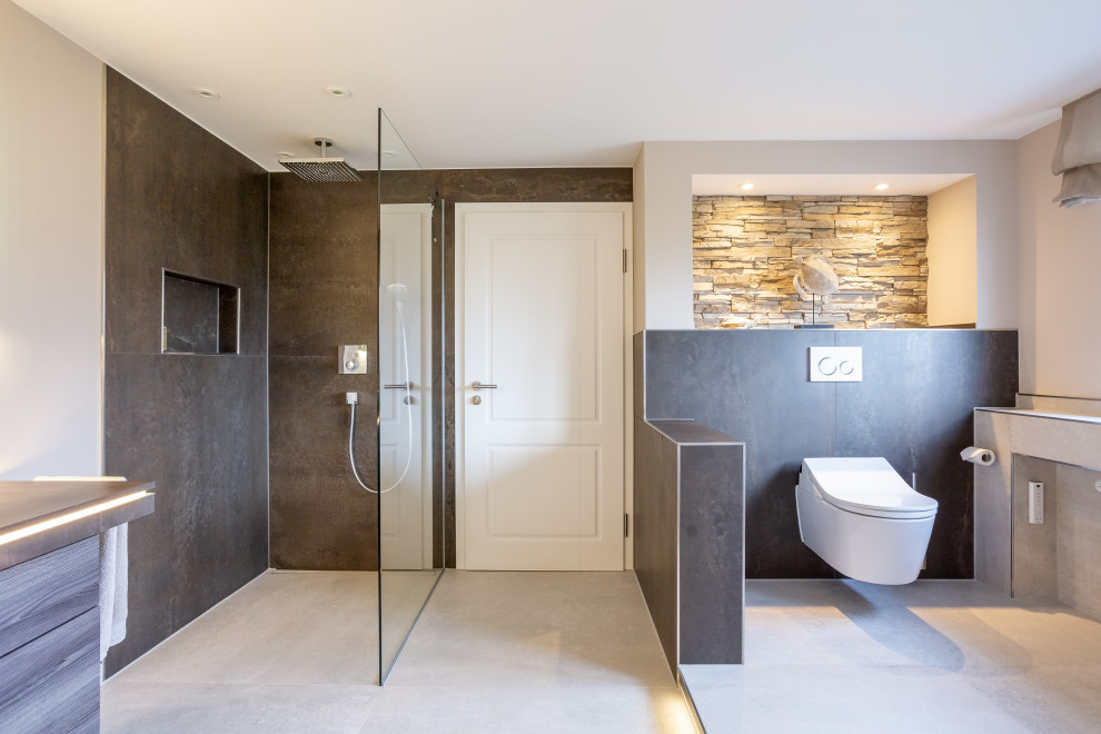 Design ideas for an expansive contemporary 3/4 bathroom in Essen with flat-panel cabinets, brown cabinets, a freestanding tub, a curbless shower, a wall-mount toilet, brown tile, metal tile, beige walls, ceramic floors, a vessel sink, wood benchtops, grey floor, an open shower and brown benchtops.