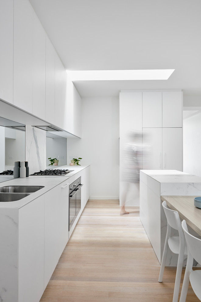 This is an example of a large modern single-wall kitchen pantry in Melbourne with beaded inset cabinets, white cabinets, marble benchtops, white splashback, marble splashback, stainless steel appliances, slate floors, with island, white floor and white benchtop.